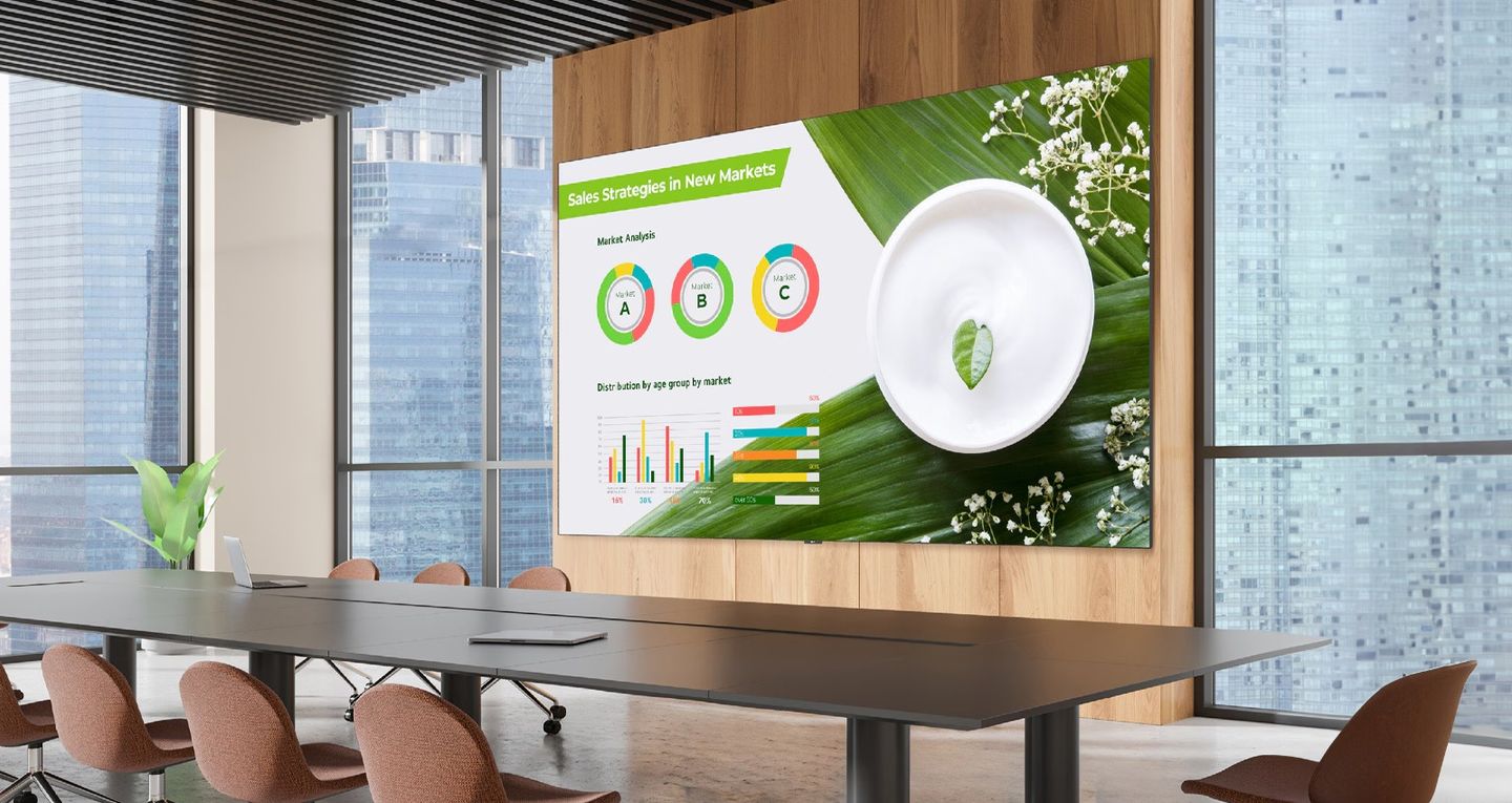 An all-in-one LED display carrying corporate content on a wood-panelled wall, seen across an open floor.